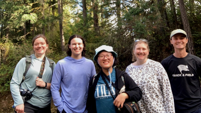 The four interns stand in a line with Director of Conservation Brittany Michalski in the forest.